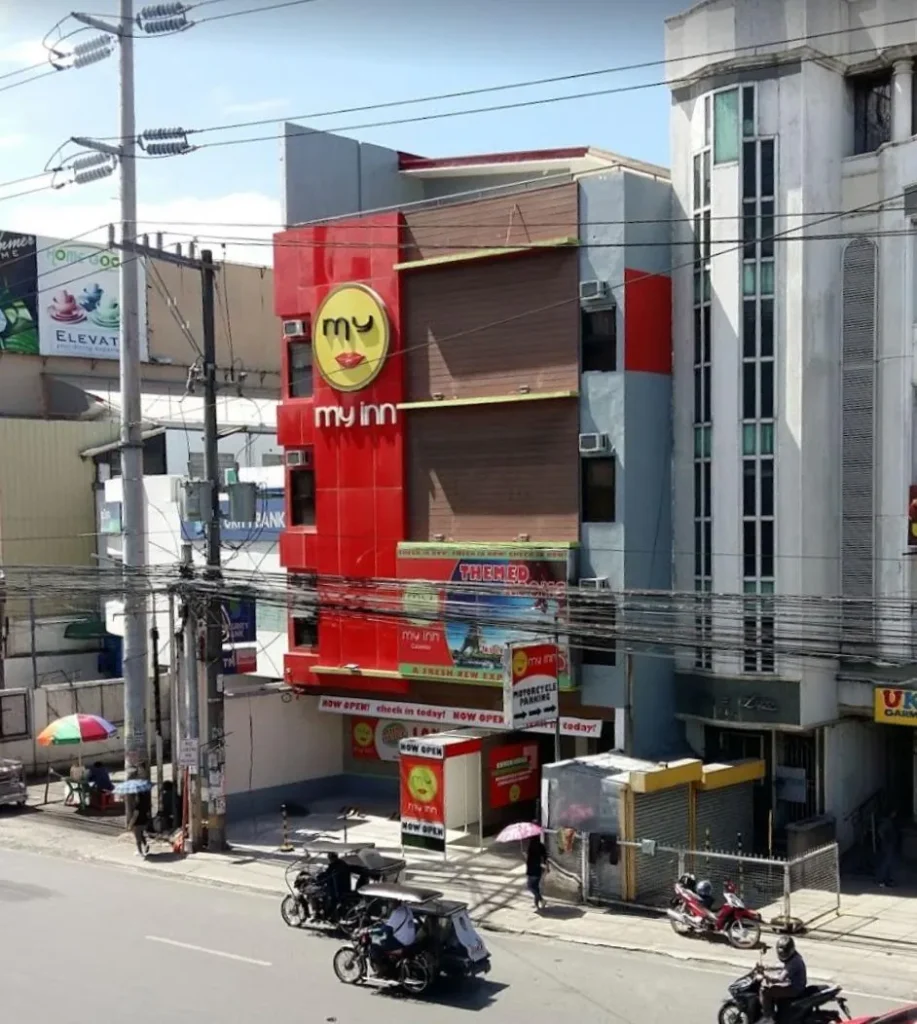 High-angle street view of the modern red, gray, and brown building facade of My Inn Calamba in Laguna, with passing tricycles and motorbikes.