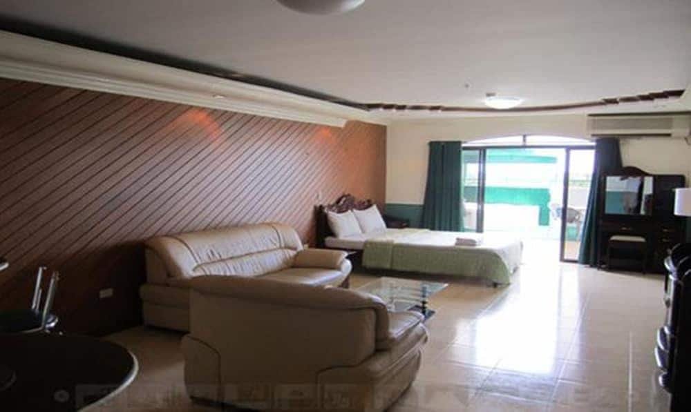 Spacious executive suite room at Natalia Hotel in Angeles, Clark, Philippines, featuring a leather sofa seating area, a large bed, a wooden accent wall, and a private balcony.