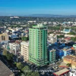 Low-angle shot of New Dawn Plus hotel in Cagayan de Oro, showing its modern multi-story concrete facade with a corner column of windows under a blue sky.