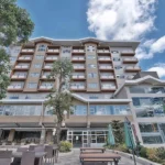 Low-angle view of the modern multi-story building facade and outdoor patio seating at Newtown Plaza Hotel in Baguio.