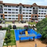 High-angle view of an outdoor playground with a bright blue safety mat in front of a mid-rise condominium building at One Oasis Davao.