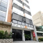 Exterior daytime view of the modern OYO 848 Dona Aurora Condotel building in Manila, Philippines, featuring white and wood-accented facade, geometric balcony grilles, and the "Dona Aurora Condotel" and OYO branding.