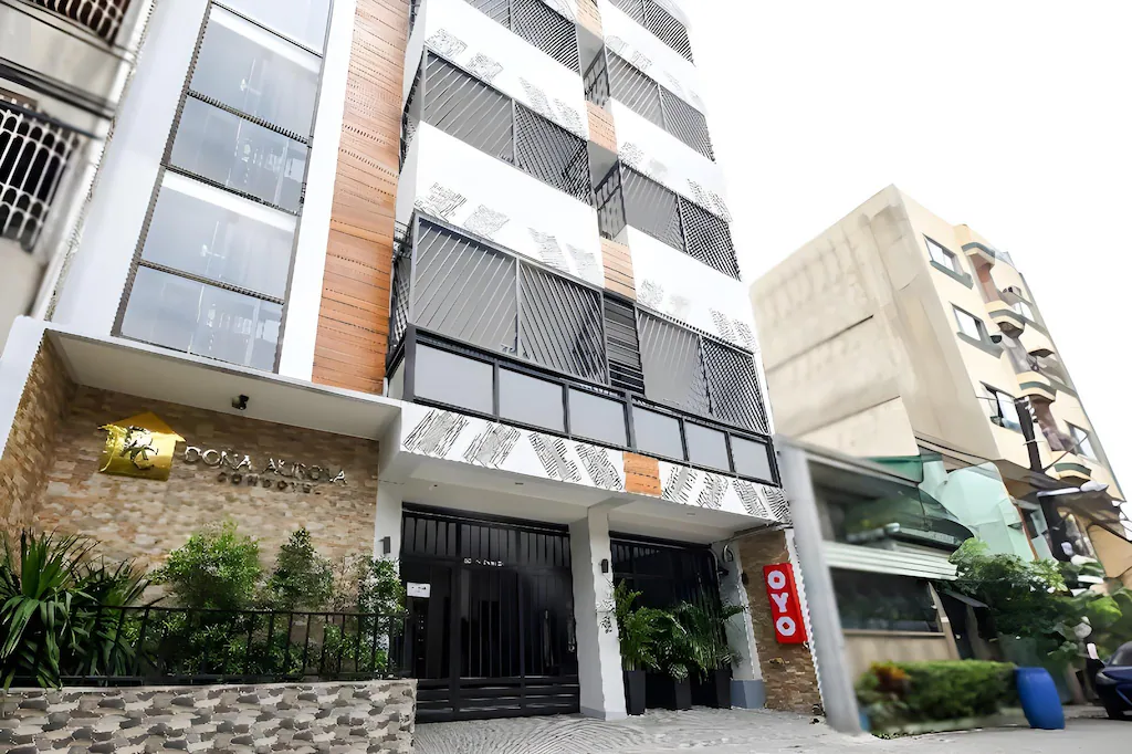 Exterior daytime view of the modern OYO 848 Dona Aurora Condotel building in Manila, Philippines, featuring white and wood-accented facade, geometric balcony grilles, and the "Dona Aurora Condotel" and OYO branding.