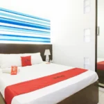 Interior view of the reception lobby at RedDoorz EL Highway Hotel Bulacan, featuring a wood-paneled front desk, green armchairs, and a tiled floor.