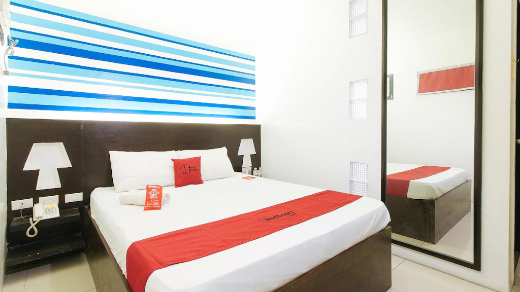 Interior view of the reception lobby at RedDoorz EL Highway Hotel Bulacan, featuring a wood-paneled front desk, green armchairs, and a tiled floor.