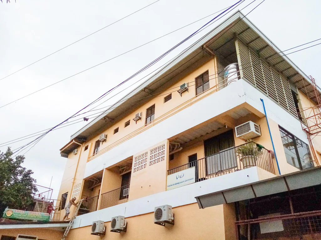 Low-angle view of the yellow and white multi-story exterior facade of RedDoorz near Baclay Drive Super Metro in Cebu, showing private balconies and aircon units.