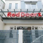 Front exterior view of RedDoorz Plus Torre de Manuel Residences 1 in Manila, showcasing a large red 3D logo above a grey security fence