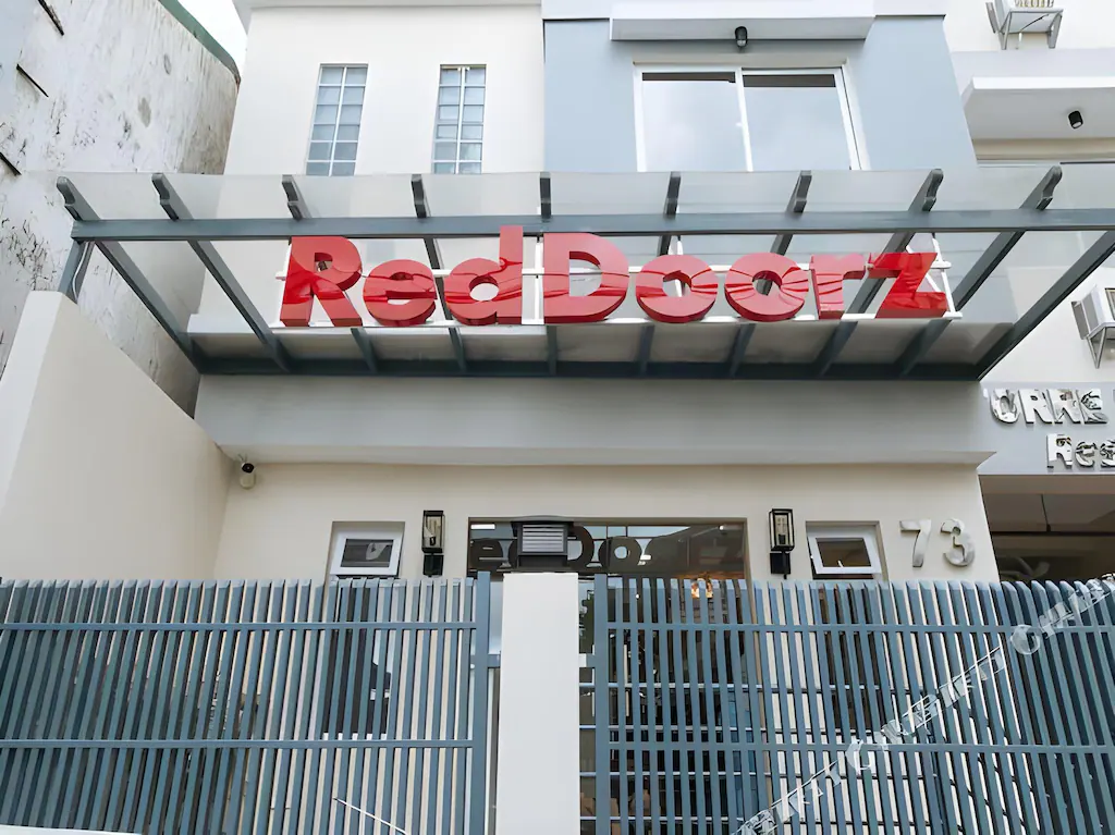 Front exterior view of RedDoorz Plus Torre de Manuel Residences 1 in Manila, showcasing a large red 3D logo above a grey security fence