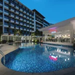 A twilight photograph of the swimming pool and Chambery Pool Bar at Savoy Hotel Boracay, with the multi-story resort building in the background.