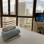 Modern luxury hotel room with a panoramic skyline view overlooking the lush Greenbelt park and high-rise buildings in Makati, Manila, Philippines.