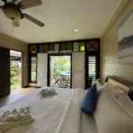 Interior view of a resort bedroom at Sol De Maria Boutique Resort, showing a large bed with white linens looking out onto a private patio and swimming pool.