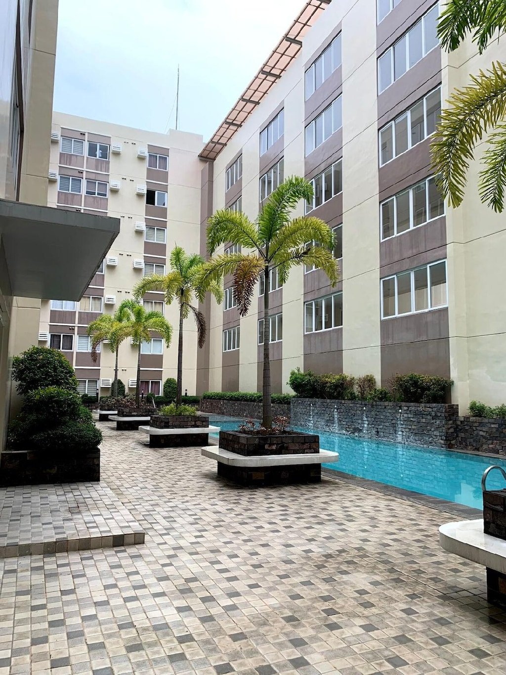 An outdoor lap swimming pool and courtyard area lined with palm trees between multi-story residential buildings at Stanford Suites 3 in Cavite.
