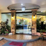 Warmly lit glass entrance of Subic Residencias hotel in Zambales, featuring stone pillars, potted plants, and a small water fountain.