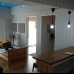 Interior view of a studio apartment at Tagaytay Prime Condotel, featuring a wooden daybed, an open kitchen bar counter, and hanging light bulbs.