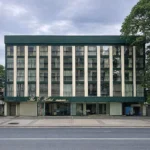 Front exterior view of The E-Hotel Makati in Manila, featuring a multi-story grid facade with dark green borders and cream columns across a paved street.