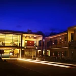 Nighttime view of the modern, two-story exterior of The Horizon Suites and Arcade in General Santos City, Philippines, showing a well-lit lobby with glass walls and a car in the driveway.