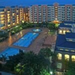 High-angle evening view of The Teal Deal condo resort complex in Manila, Philippines, featuring multiple swimming pools, a tiled courtyard plaza, and illuminated mid-rise apartment buildings.