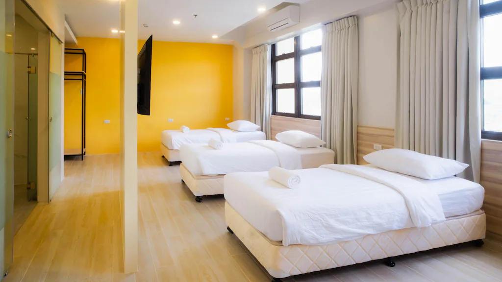 A brightly lit, modern triple room interior at Treewoods Residences in Cebu City, Philippines, featuring three single beds with white linens, a bright yellow accent wall, a wall-mounted TV, and large windows with curtains and air conditioning.