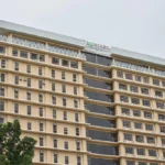 The exterior view of Treewoods Residences, a multi-story hotel and serviced apartment building in Apas, Cebu City, Philippines, featuring a tan colored facade, tinted windows, and balconies under a bright overcast sky.