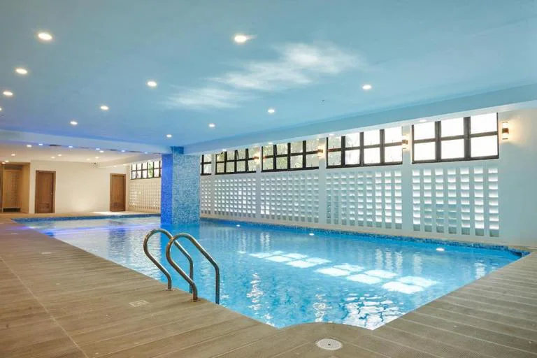 The spacious indoor swimming pool at Treewoods Residences in Cebu City, Philippines, featuring clear blue water, a wood-look tiled deck, modern overhead lighting, and decorative white ventilation bricks.