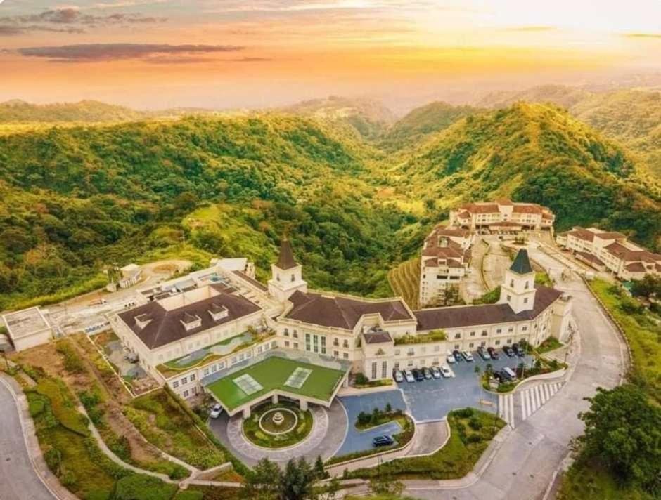 Aerial view of Twin Lakes Condominium buildings nestled in the lush green hills of Laurel, Batangas, under a golden sunset sky.