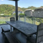 Modern living room interior of a two-bedroom condo at Pico de Loro in Nasugbu, showing a large grey sectional sofa, wooden wall panels, and balcony access.