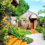 Exterior view of a unique, thatch-covered dome cottage at UNWND Boutique Hotel Dumaguete in the Philippines, surrounded by a lush tropical garden and paved pathways.