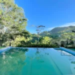 An outdoor infinity swimming pool reflecting a vibrant blue sky and green trees with mountains in the background at Victoria's Peak - El Cinco Farmville and Resort.
