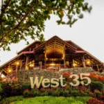 Low-angle view of the large wooden main pavilion and landmark text sign at West 35 Eco Mountain Resort in Balamban, Cebu.