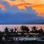 Stunning sunset over Subic Bay at Whiterock Beach Hotel and Waterpark in Zambales, Philippines, featuring an illuminated I Heart Whiterock sign, palm trees, and coastal mountains.