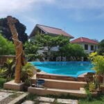 Elevated outdoor swimming pool at Wonderfarm Villa in Batangas, featuring a rustic wooden post shower and white vacation houses in the background.