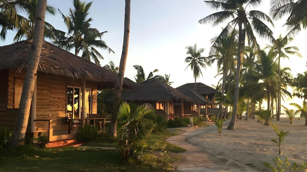 Crystal clear turquoise ocean water and powdery white sand beach in front of native-style cottages at Kota Beach Resort in Bantayan Island, Cebu, Philippines.