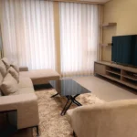 Modern living room area of the Family Junior Suite at Bayprime Hotel, featuring a large beige L-shaped sectional sofa, a flat-screen TV, and a plush area rug.